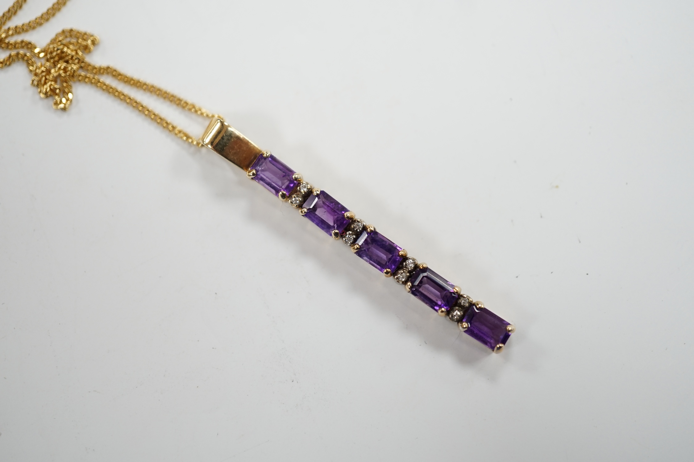 A modern yellow metal, amethyst and diamond chip set line pendant, 47mm, on an 18ct gold fine link chain, 38cm, gross weight 6.4 grams.